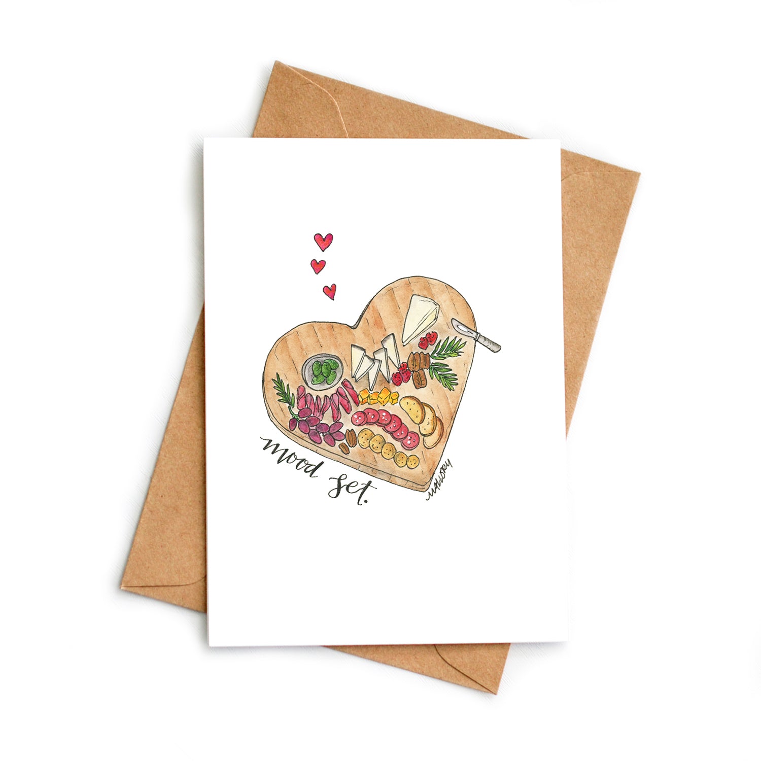 Image depicts a charcuterie board in the shape of a heart with fancy cheeses, cured meats, berries and herbs. Little red hearts are above the charcuterie board. "Mood set" is hand-lettered on the card to signify "setting the mood" for Valentine's Day.