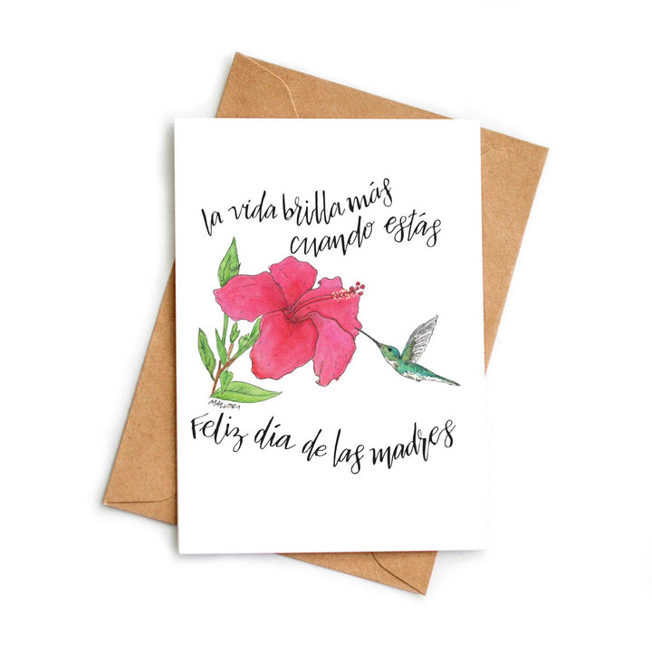 Greeting card with pink flower and hummingbird illustration on a white background with brown envelope.