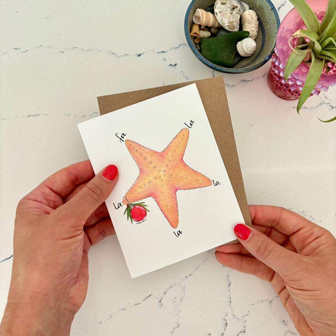 Person holding a card with a starfish illustration on a marble surface.