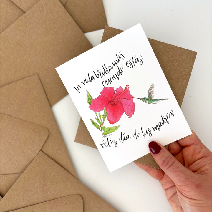 Card with floral design and text held by a hand, surrounded by brown envelopes.