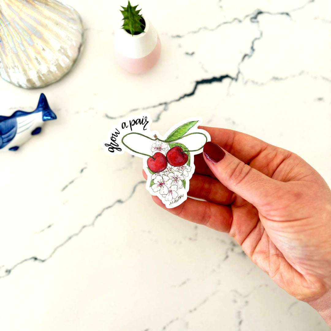 Hand holding a sticker with cherries and text on a marble surface