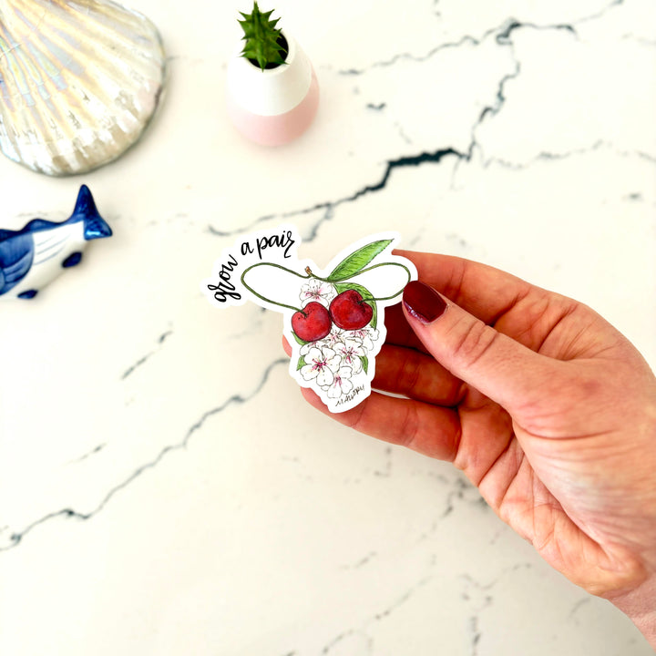 Hand holding a sticker with cherries and text on a marble surface