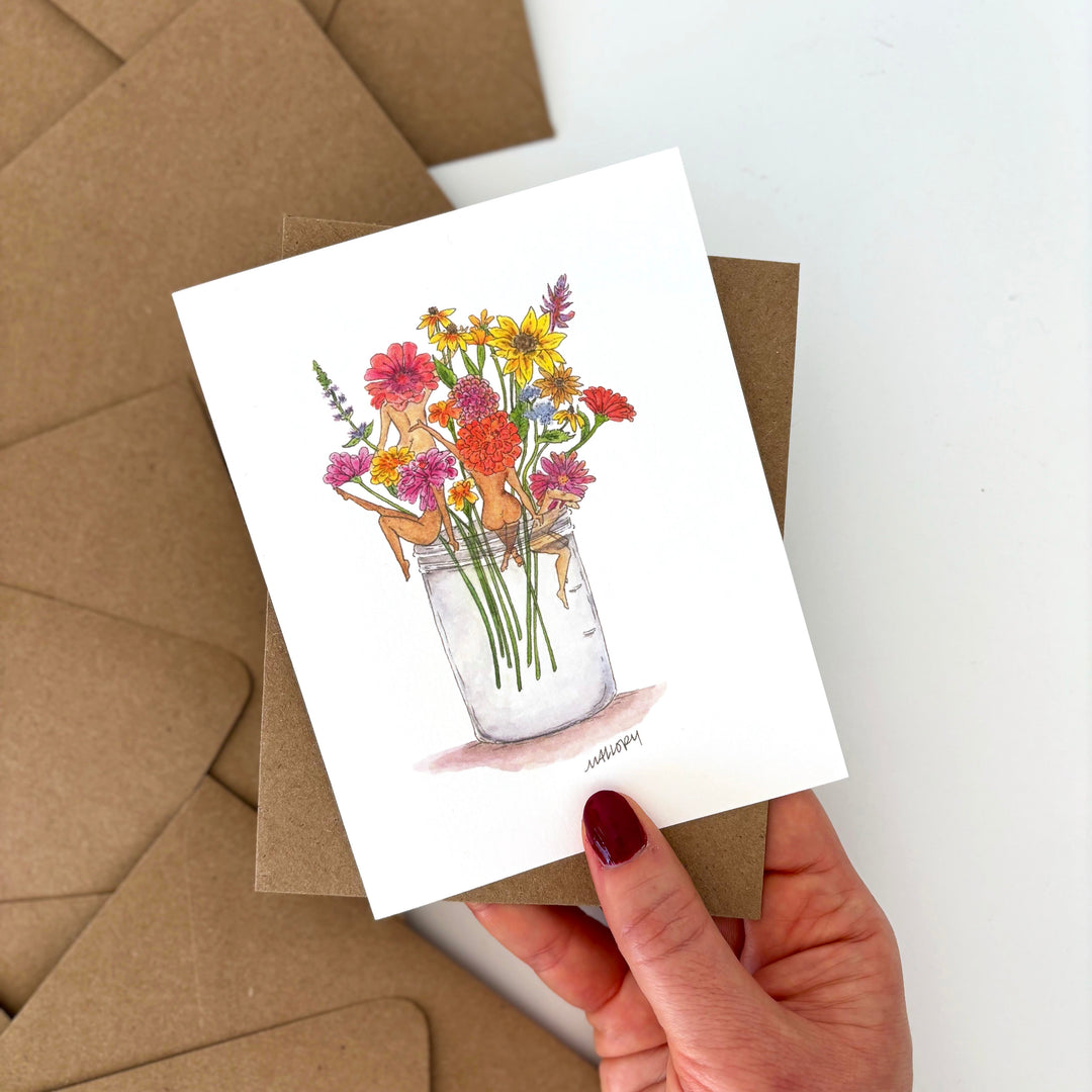 Greeting card with floral design held by a hand, surrounded by brown envelopes.