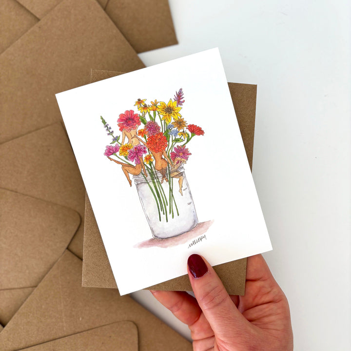 Greeting card with floral design held by a hand, surrounded by brown envelopes.