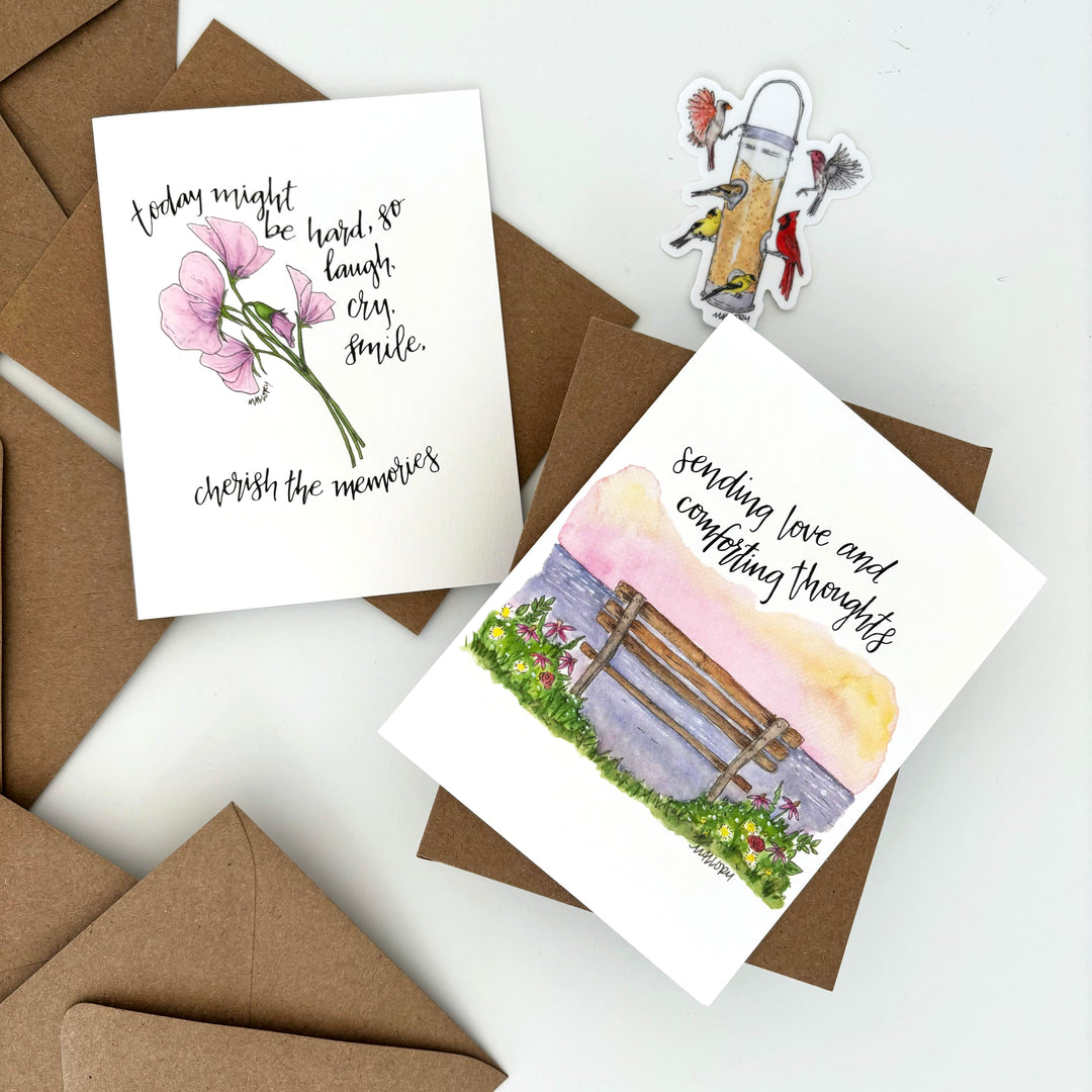 Two sympathy cards with floral designs and text on a white surface with brown envelopes.