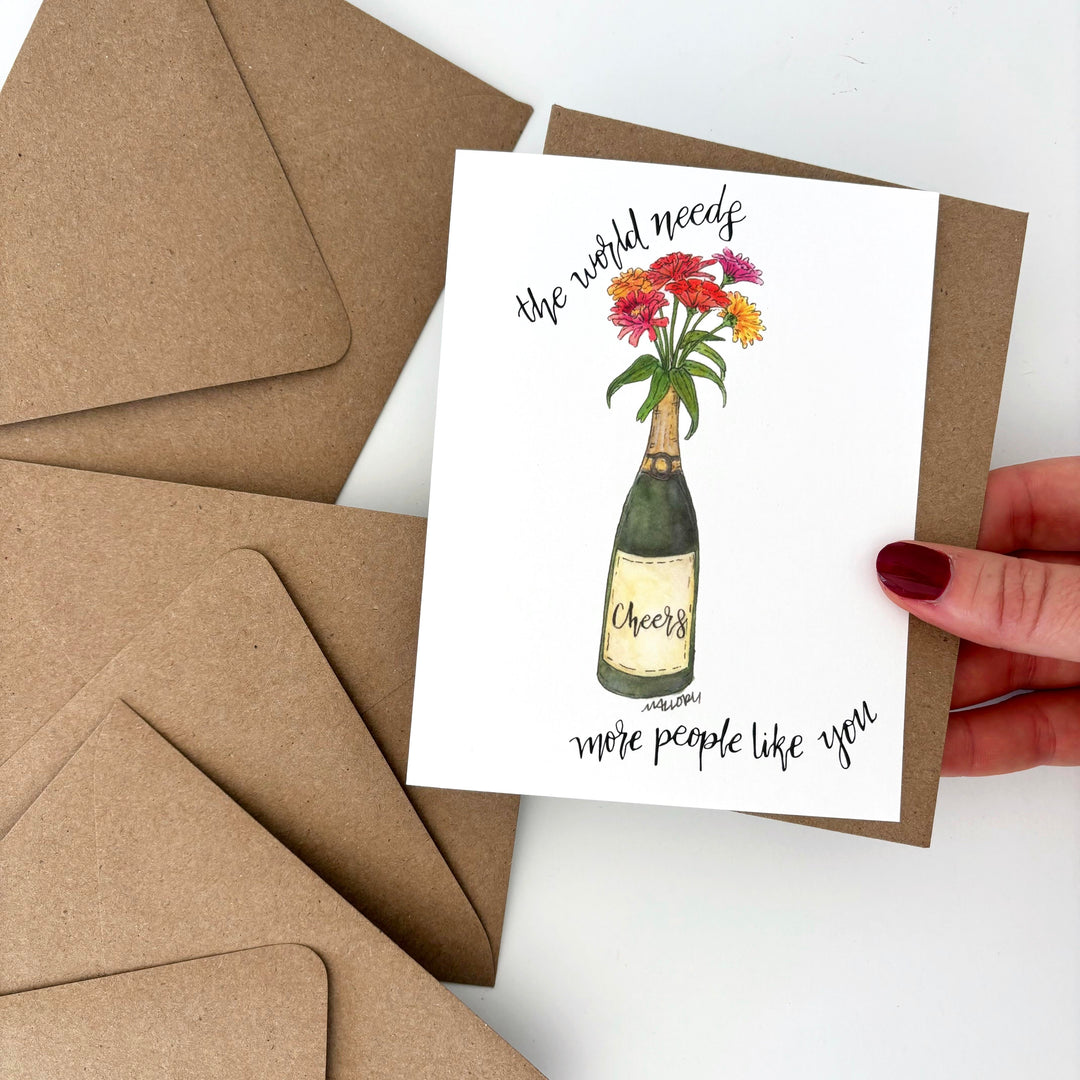 Greeting card with champagne bottle and flowers design held by a hand, surrounded by brown envelopes. Text reads, "the world need more people like you".