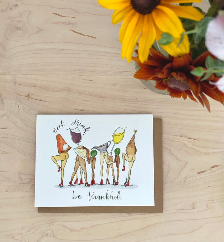 Thanksgiving or Friendsgiving card depicts a funny image with Thanksgiving food with legs. The food is dancing with wine and the phrase, "eat. drink. be thankful." is hand-lettered.