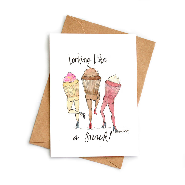 Image of greeting card on kraft recycled envelope. Card is illustrated with a vanilla cupcake, a chocolate cupcake and a red velvet cupcake with butts. The card reads, "Looking like a snack!".