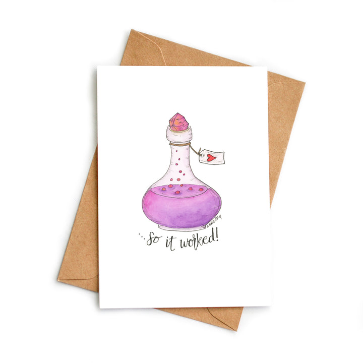 Image of a fancy bottle with a purple and pink love potion with pink bubbles. A pink, glowing crystal seals the bottle with a small tag with a red heart. The words, "...so it worked!" are hand-lettered below to show the love potion worked.