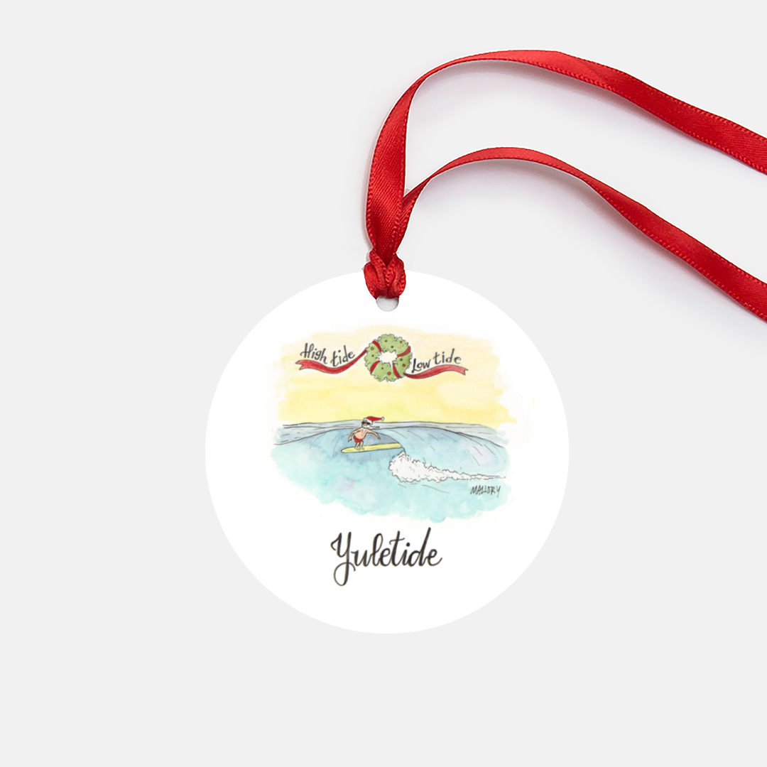 White metal ornament is in the shape of a circle and comes with a red satin ribbon for hanging. Ornament features a watercolor illustration of a Santa surfing on a wave and reads, "High tide, low tide, yuletide".