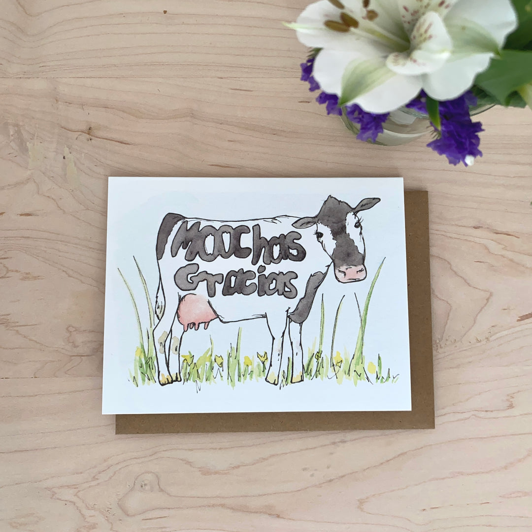 Image of a thank you card with a black and white cow in a field. The words "muchas gracias" are hidden in the cow's spots.